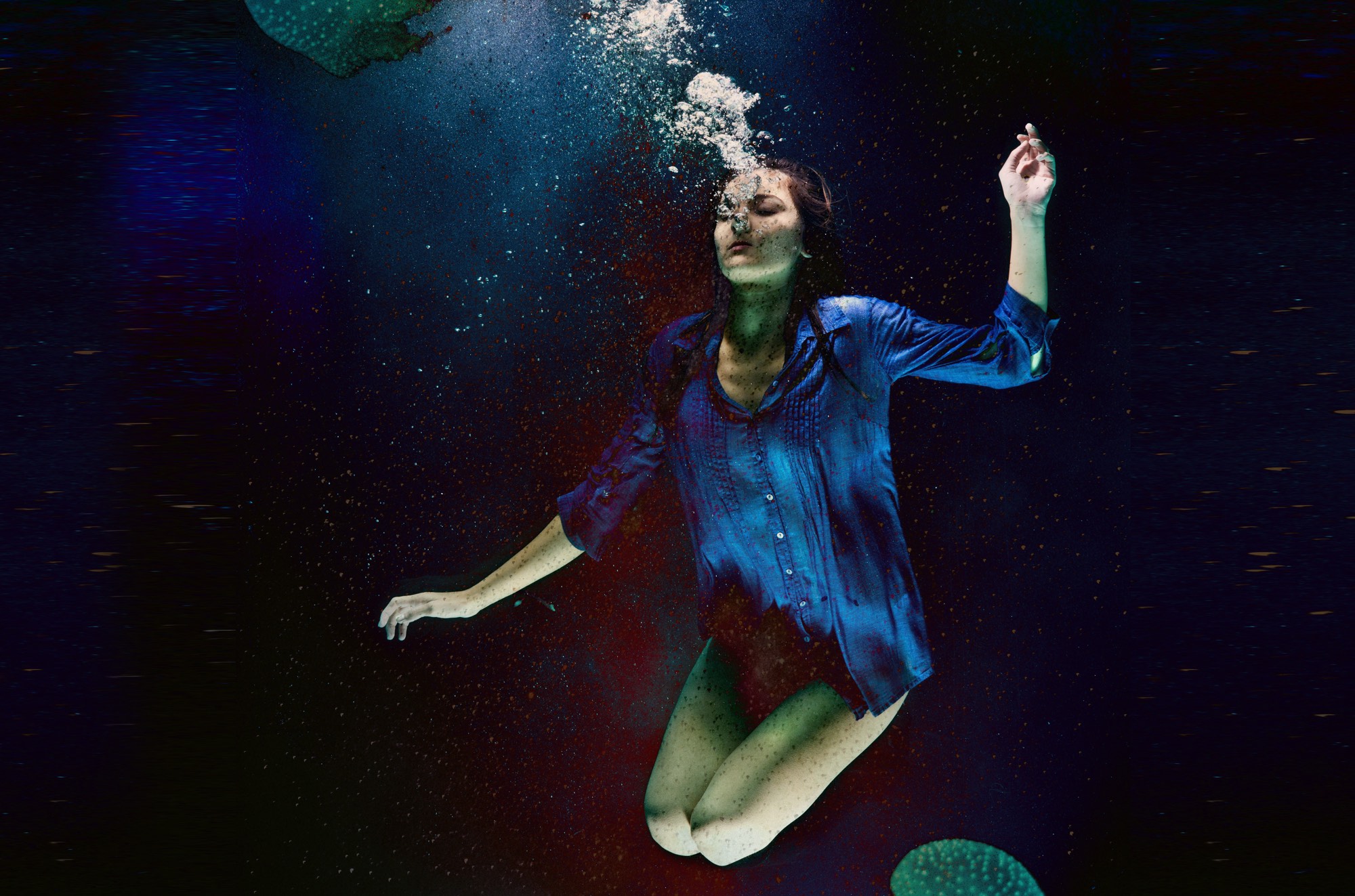A women is underwater in darkness. Bubbles ascape hare mouth.